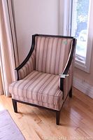 Front angle view of wood framed chair with beige, brown, and muted red striped fabric upholstery. Shows padded seat cushion and curved armrests.