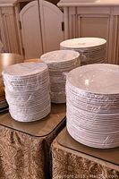 Stacks of white plates wrapped in plastic film on a table.