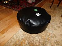 View from above showing round black faux leather footstool with slight puffed top surface and smooth sides.