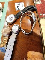 Four wristwatches displayed on wooden table showing various styles including leather and metal bands