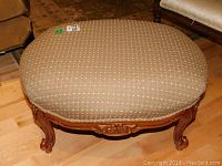 Top view of round beige upholstered ottoman showing diamond patterned fabric with gold accents and wooden base.