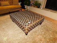Angled view of the upholstered coffee table in living room setting showing top and side pattern.