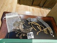 Full view of the jewelry pieces on the table showing the wide silver-tone statement necklace with multiple coin charms, gold-tone beaded necklace, silver chevron bracelets, and other pieces.
