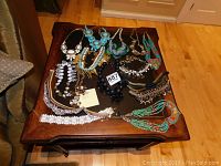 Photo of 14 assorted necklaces with various designs, colors including turquoise, coral, black, white, and gold.