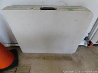 Folded view of the 72 inch white folding table showing the carrying handle and the soiled surface.