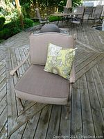 Front view of metal patio chair with brown cushions and floral pillow on wooden deck.