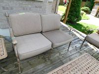 Front-facing view of metal patio love seat with beige cushions on wooden deck.