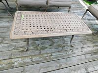 Rectangular cast metal table on wooden deck showing lattice top and scroll border.