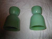 Two green Fire King egg cups viewed from a side angle on a quilted surface, showing color and form.