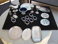 Full set of silver plated serving pieces displayed on black cloth including trays, salt cellars with cobalt blue glass inserts, goblets, gravy boat, and decorative pierced plates.