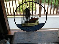 Full view of circular stained glass fishing troller window hanger on porch railing with wooden table below.