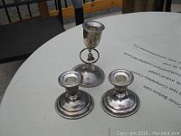 Photo showing the three silver candle holders on a white round table from a higher angle.