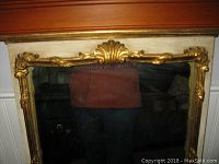 Front view of ornate gold framed mirror showing shell and floral motifs and the reflective glass surface.
