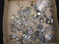 Cardboard tray with scattered metal-tone and enamel jewelry bits: hoops, charms, pendants, brooch fragments.