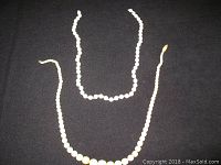 Photo showing two ivory or bone bead necklaces laid out on a flat surface, one with larger beads showing yellowing, the other with smaller uniform white beads.