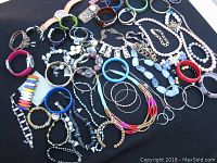 Photo showing a collection of assorted vintage costume jewelry items including bracelets, bangles, and necklaces displayed on a dark cloth.