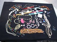 Full view of vintage costume jewelry lot including necklaces, bracelets, earrings, brooches, and wristwatches arranged on black background.