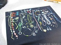 Top view showing the full assortment of vintage costume jewelry including necklaces, earrings, bracelets, and pins laid out on a black cloth.