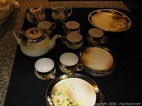 Full view photo of Meito China tea set including plates, teapot, cups, sugar bowl, creamer, and tray displayed on a black surface.