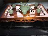 Top view of wooden ceremonial tea tray with 6 small ceramic cups and teapot on top, showing carved legs and Chinese characters on tray.