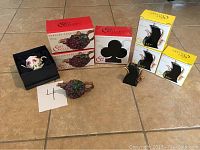 Eight Fitz and Floyd mini teapots in original boxes and unpackaged displayed on floor; includes grape, saxophone, club shapes.