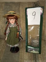 Front view of the Anne of Green Gables doll standing next to its original green display box with a clear window.