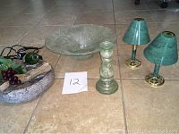 Photo shows large textured glass bowl, two brass candle holders with green shades, tall green glass candle holder, and decorative tabletop fountain base on tiled floor.
