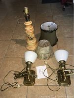 Photo showing multiple lamps and shades including a painted porcelain lamp base, a brass lamp, and three lampshades.