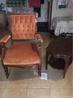 Antique Eastlake captain chair with orange tufted velvet upholstery and carved wooden frame next to wooden side table