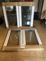 Four new white framed windows stacked in a room, two standing upright boxed, two lying flat, showing size and packaging.