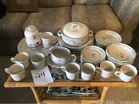 Full set of stoneware dishes on table showing cups, saucers, plates, bowls, and serving pieces with floral bird design.