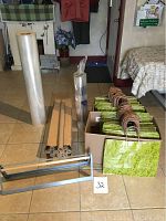 Overview of gift wrap related items including plastic wrap rolls, kraft paper rolls, shopping paper bags in a box, and a metal gift wrap paper dispenser on tile floor.