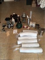 Full lot view showing samovar, whip cream maker, latte dispenser, jars, canister, sifter, cups lids and vases on tiled floor.