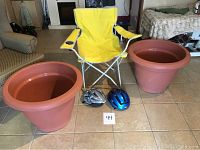 Two large plastic flower pots, one cracked, yellow kids chair between them with two bicycle helmets in front.