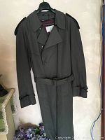 Full view of dark trench coat with belt, double-breasted front buttons, and epaulets on shoulders.