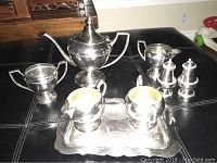 Full overview of 8 piece Victorian silver plated tea set including teapot, milk and sugar pots, salt and pepper shakers, and tray on a black surface.