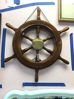 Front view of wooden ship wheel showing the full wheel with six handles and brass centerpiece.