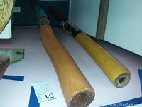 Pair of Australian didgeridoos laid out flat showing two wooden wind instruments, one with blue Aboriginal designs, the other yellowish with black and white band.