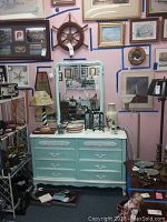Full view of the vintage painted dresser in turquoise blue with white trim surrounded by other items in the background.