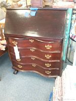 Front view of antique wooden secretary desk with slant-top closed, four curved front drawers with brass handles, and claw feet.