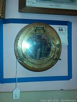 Front view of a vintage wood and brass porthole mirror with reflective glass and brass fittings.