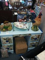Overview of lot: painted wooden furniture, glass display cube with plate inside, ceramic rooster, cast iron horse and carriage, and John Deere decor items on top of furniture.