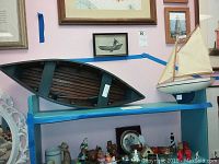Wooden rowboat and sailboat displayed on a blue shelf with various other nautical-themed decor items around them.