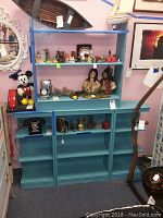 Full view of the four piece blue painted shelving unit with various collectibles displayed, including a model boat, figurines, a vintage telephone, and other decorative objects.