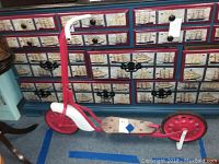 Full side view of the vintage red and white scooter with wooden footboard and solid rear wheel.