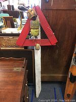 Full view of the vintage channel marker standing upright against furniture with the red triangular frame, white post, and attached yellow buoys with fishing net draped.