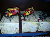 Three Coca Cola collectible model vehicles on their original boxes on a shelf.