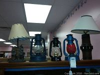 Overview of three lanterns and two table lamps arranged on a surface in a room.