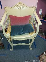 Front view of the vintage cream-colored Art Deco chair with two velvet pillows, showing decorative carved details on the backrest and armrests.