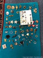 Full view of costume jewelry collection spread on blue cloth showing various pins, brooches, and stick pins arranged for display.